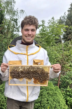 Imker Philipp Harde im Imkeranzug mit einer Wabe voller Bienen