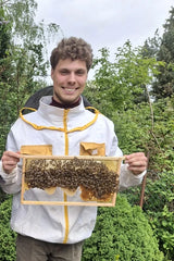 Imker Philipp Harde im Imkeranzug mit einer Wabe voller Bienen
