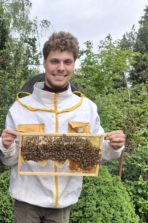 Imker Philipp Harde im Imkeranzug mit einer Wabe voller Bienen