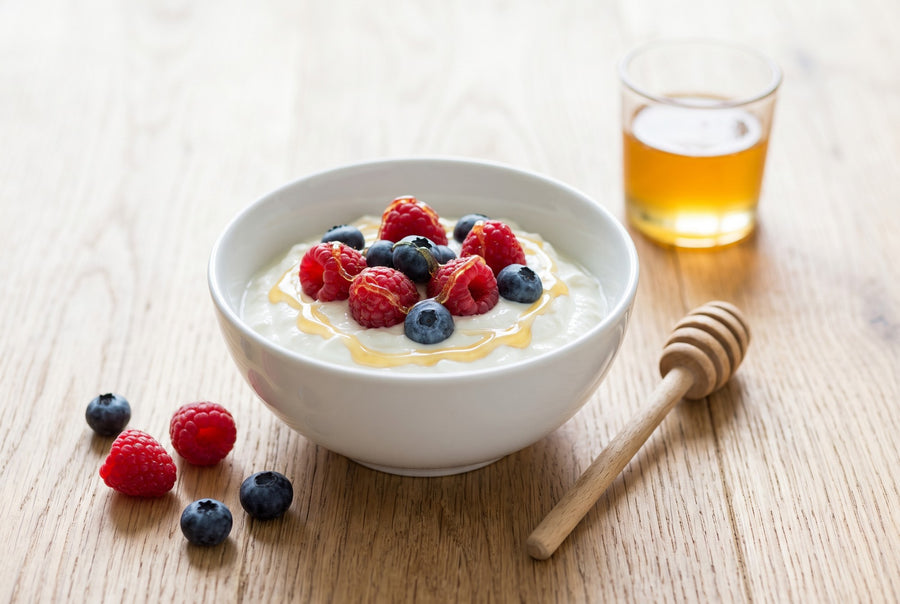 Quark mit Himbeeren, Heidelbeeren und Honig in einer weißen Schale (KI-generiert)